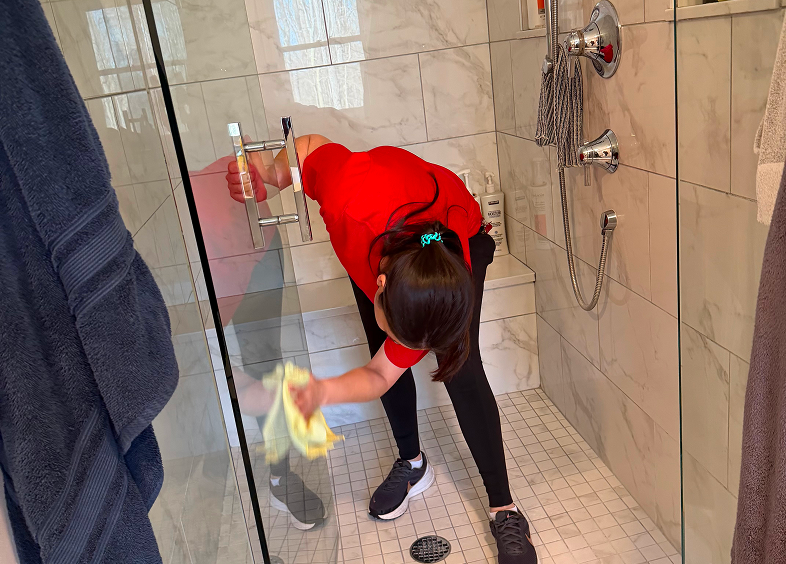 Person cleaning a glass shower door with a cloth.
