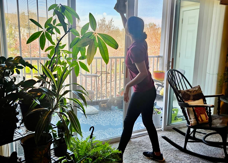 Person watering plants near a glass door in a cozy room.