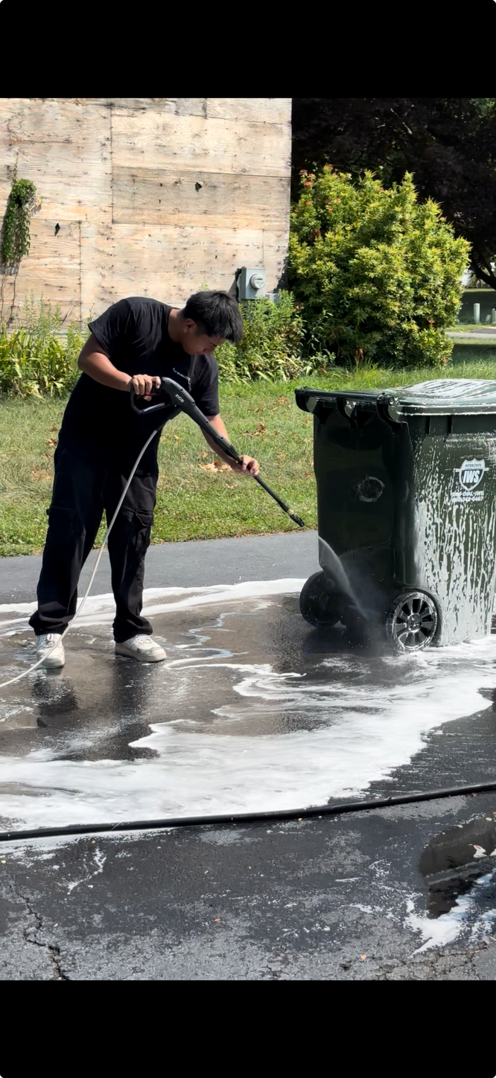 Person power washing a large trash bin outdoors.