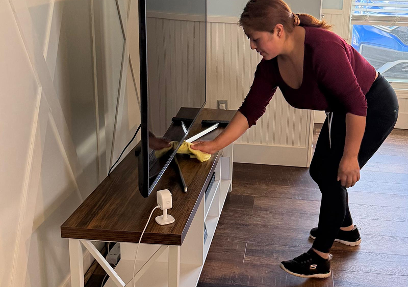 A woman dusting a TV stand with a cloth in a living room.