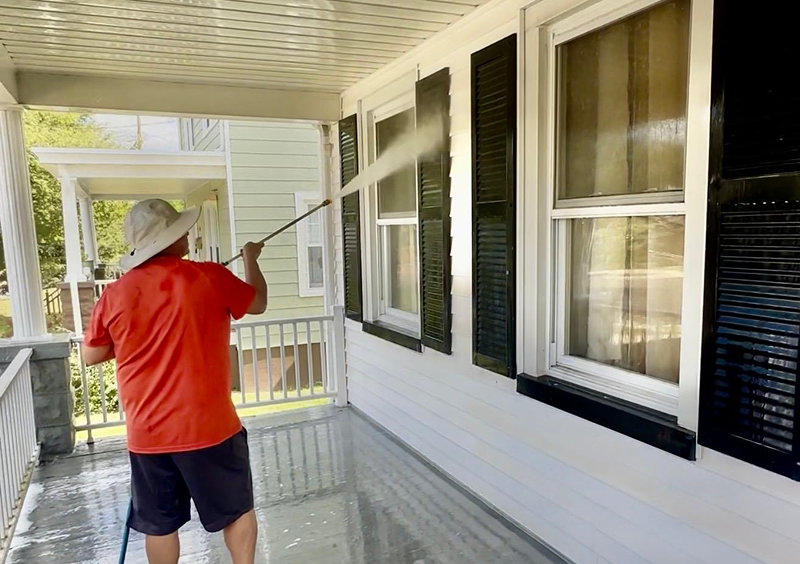 Person power washing house exterior on porch.