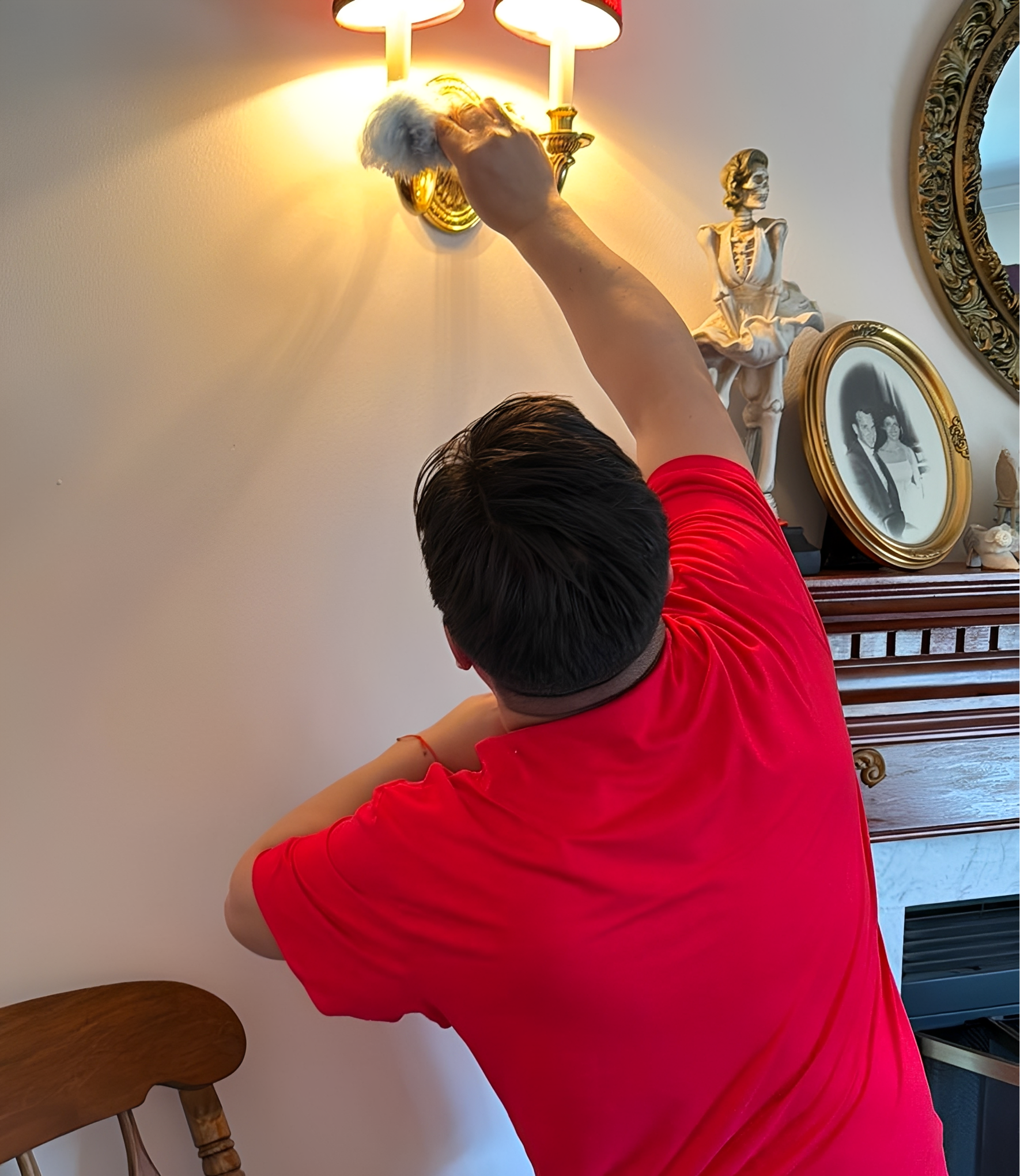 Person dusting a wall sconce with duster.